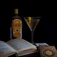 Vesper Martini cocktail, an open book, a deck of James Bond 007 playing cards and a bottle of Gordon's gin on a table with a dark background