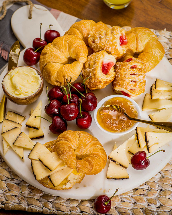 Plateau déjeuner avec fromages, cerises croissants, danoises, confitures et plus