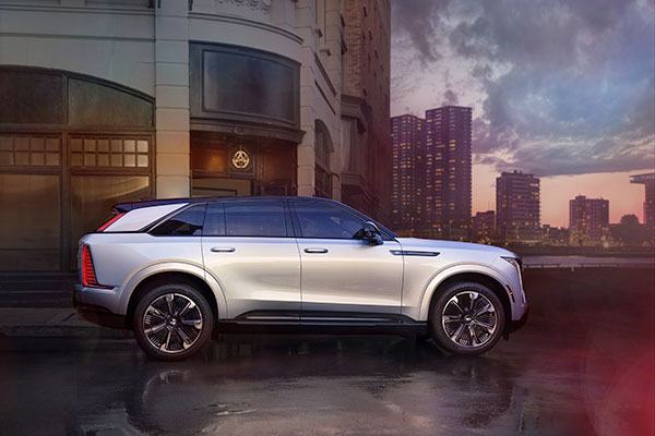 Vue latérale complète du Cadillac Escalade IQ 2025 en éclat d'argent métallisé la nuit au coucher du soleil.